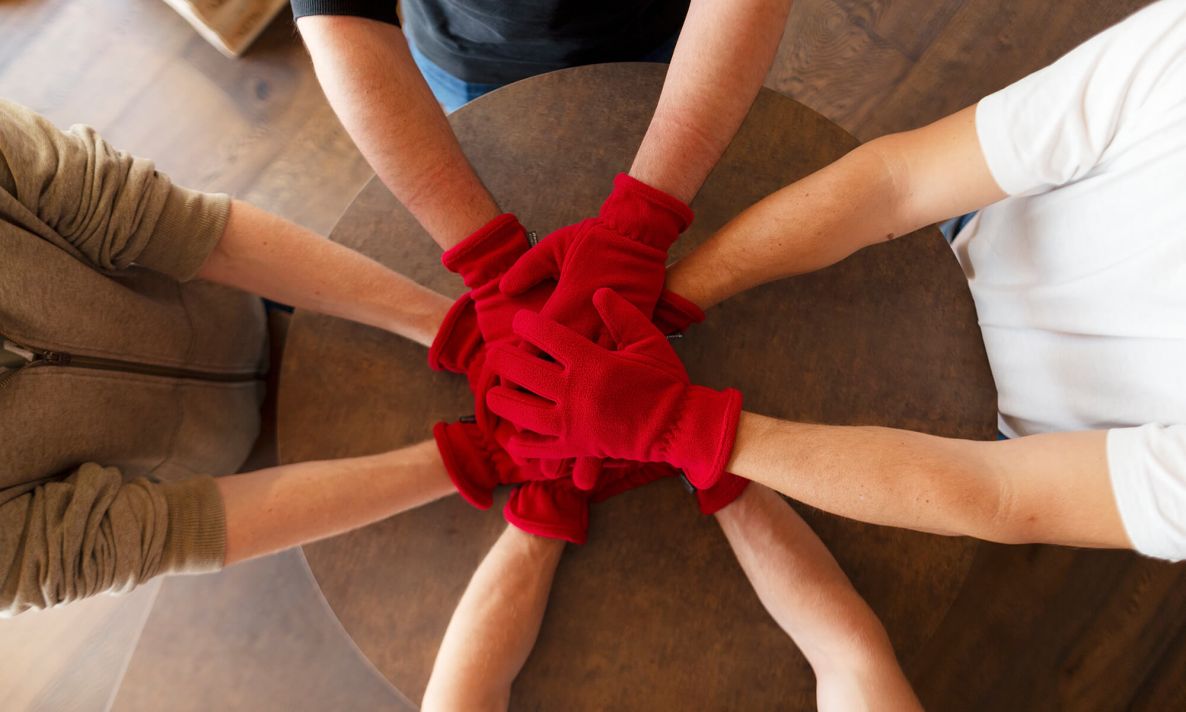 8 Hände übereinander in roten Handschuhen als Symbol für Team